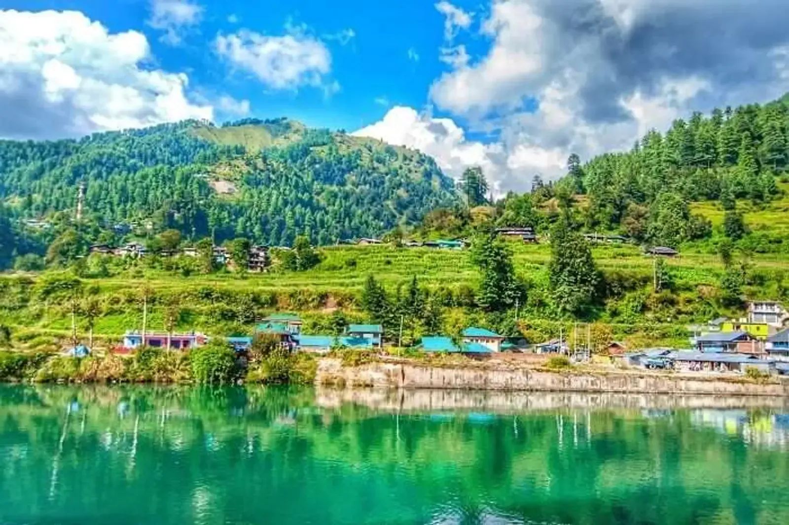 A turquoise reservoir held in a wooded valley with a scatter of village buildings along the shoreline.