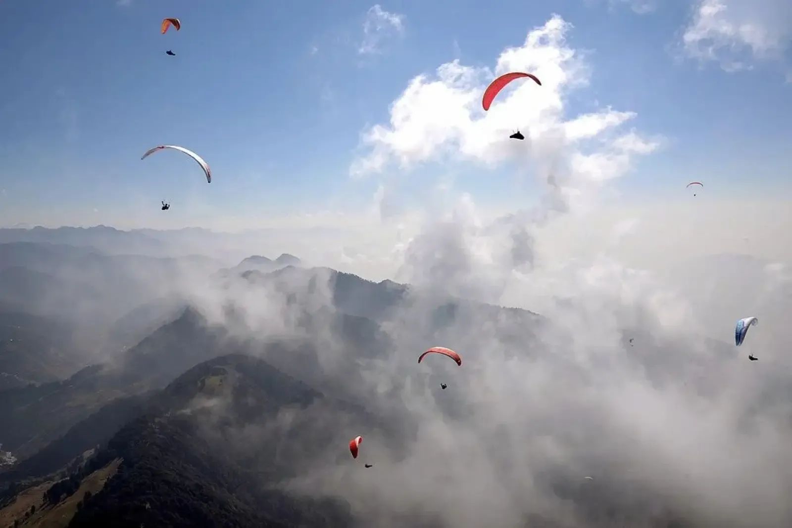 Paragliders climbing in a line above a bank of cloud with the dark ridge below them.
