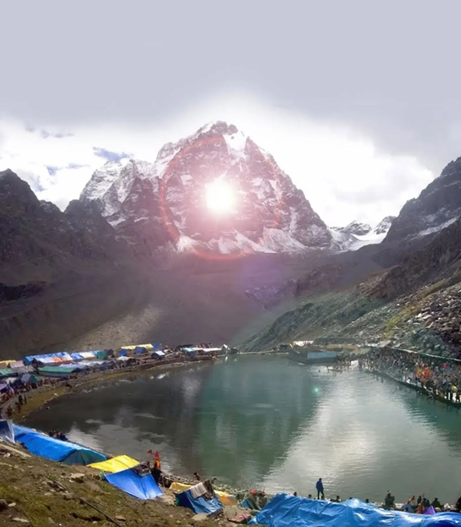 A snow peak catching the sun above a high lake with pilgrims' tarpaulin shelters pitched along the shore.