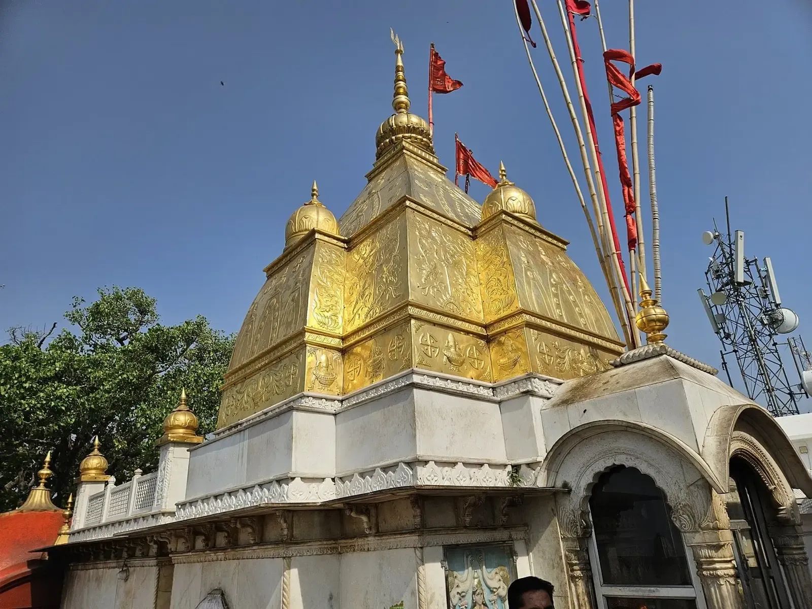 A gilded temple spire with red pennants flying from its mast against a blue sky.
