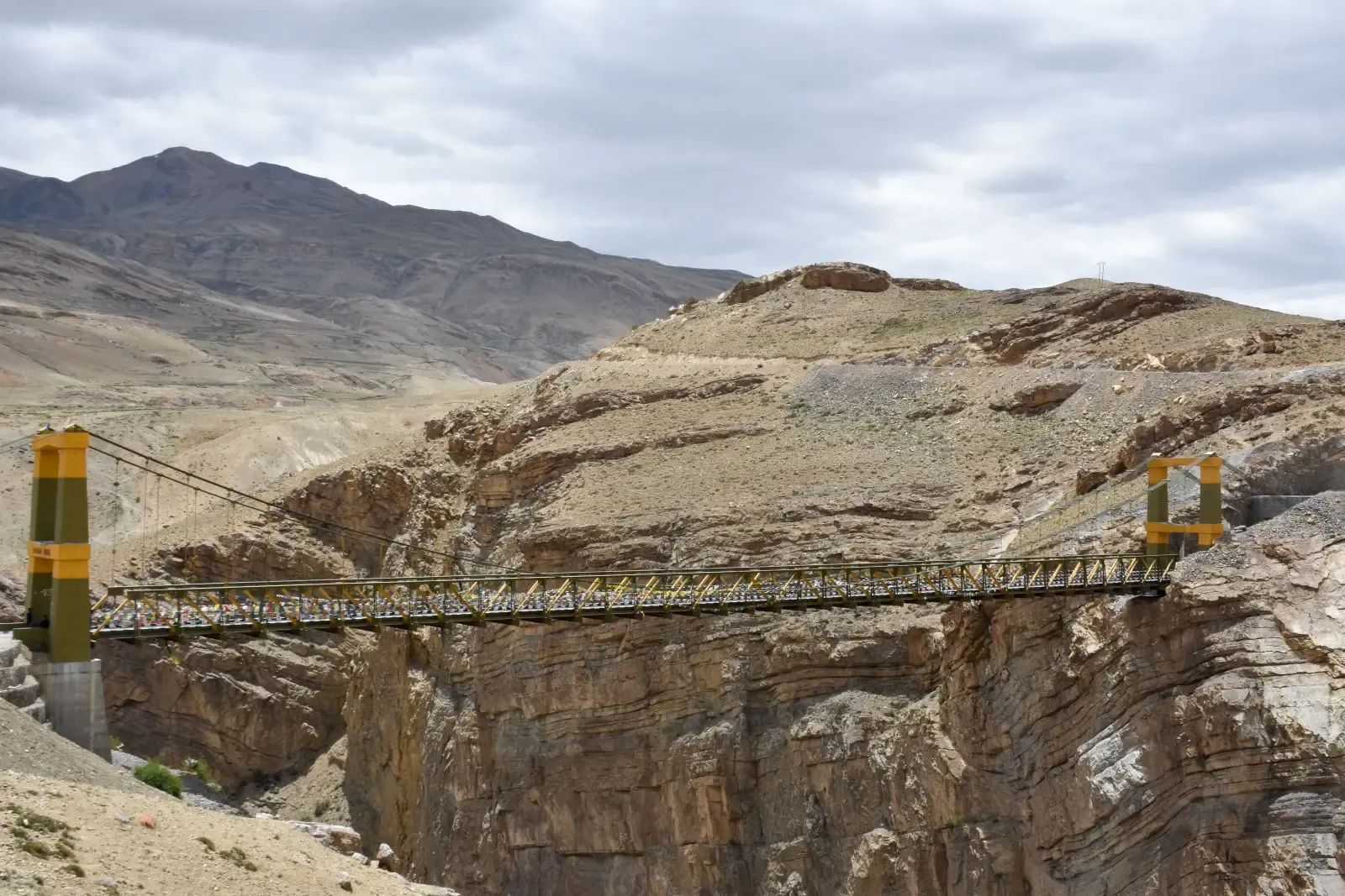 A suspension bridge carrying a single lane across a deep gorge cut in bare rock, the canyon dropping away under the deck.
